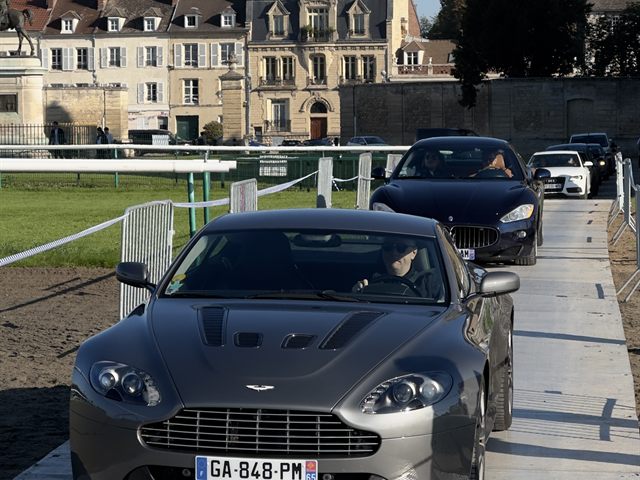 Une Aston Martin grise devant un château.