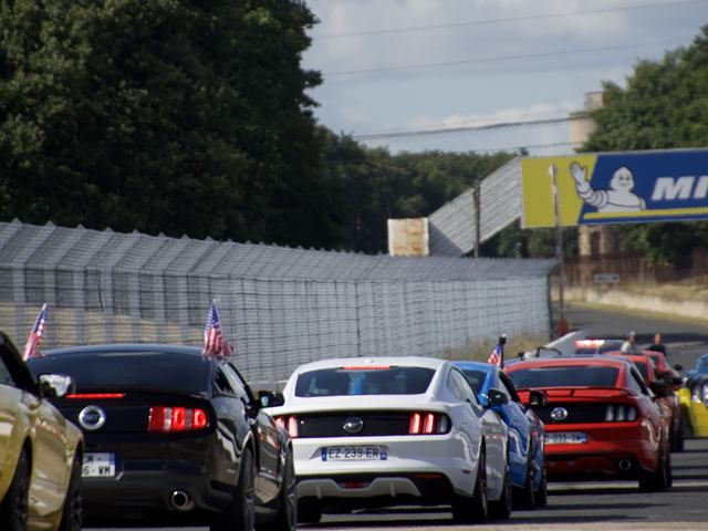 Une file de voitures le long d'un circuit, drapeaux au vent.